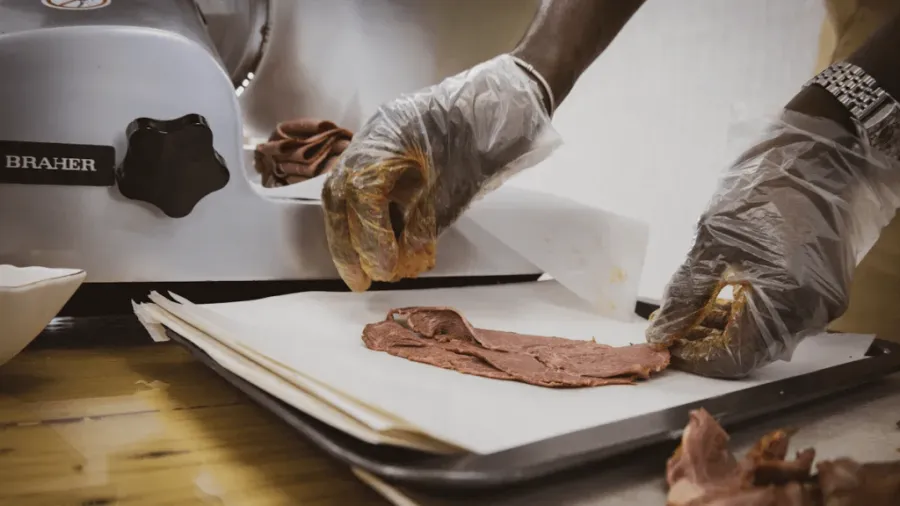 Thin deli meat being laid out by two hands.