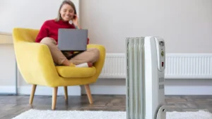A lady in cozy clothes sitting on a comfortable chair next to a portable diesel heater placed on a white colored rug
