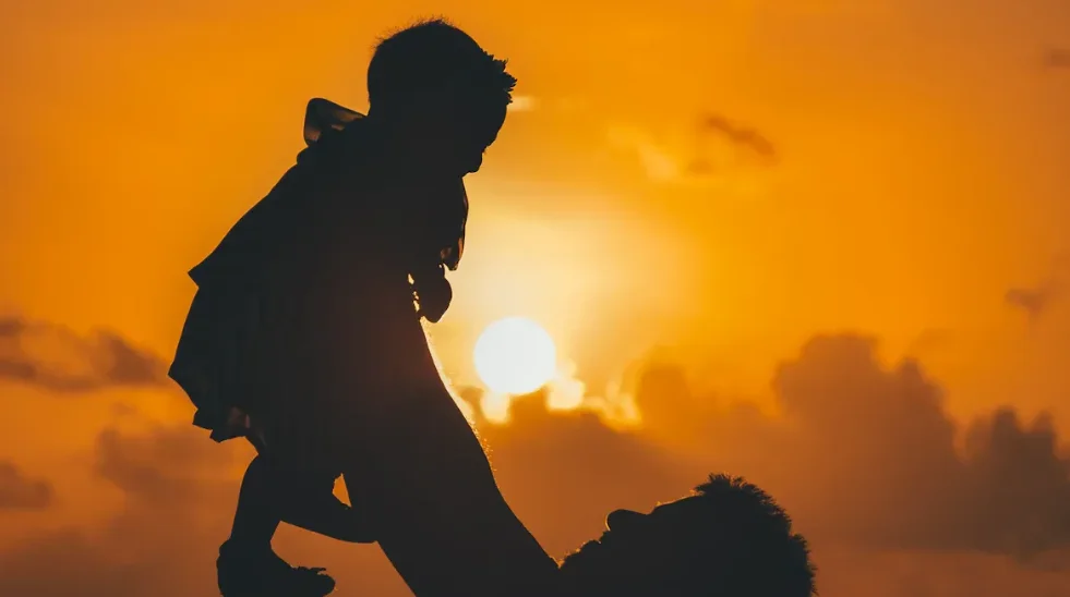 A father holding up his child in front of a sunset