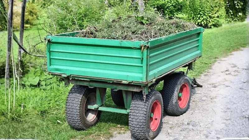 dump trailer with four wheels loaded with grass and dead tree leaves