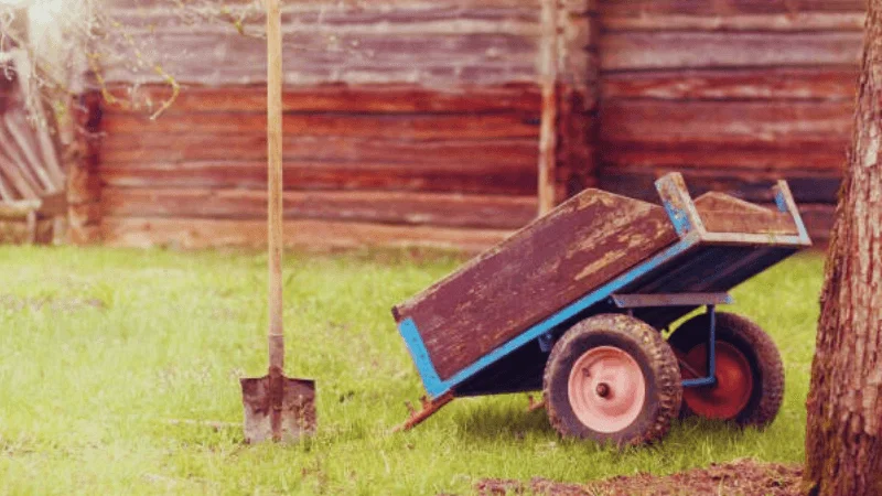 hand-pulled garden trailer dump cart next to a shovel in a garden