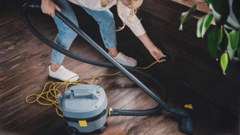 woman plugging in the cord for her vacuum cleaner into an electrical outlet