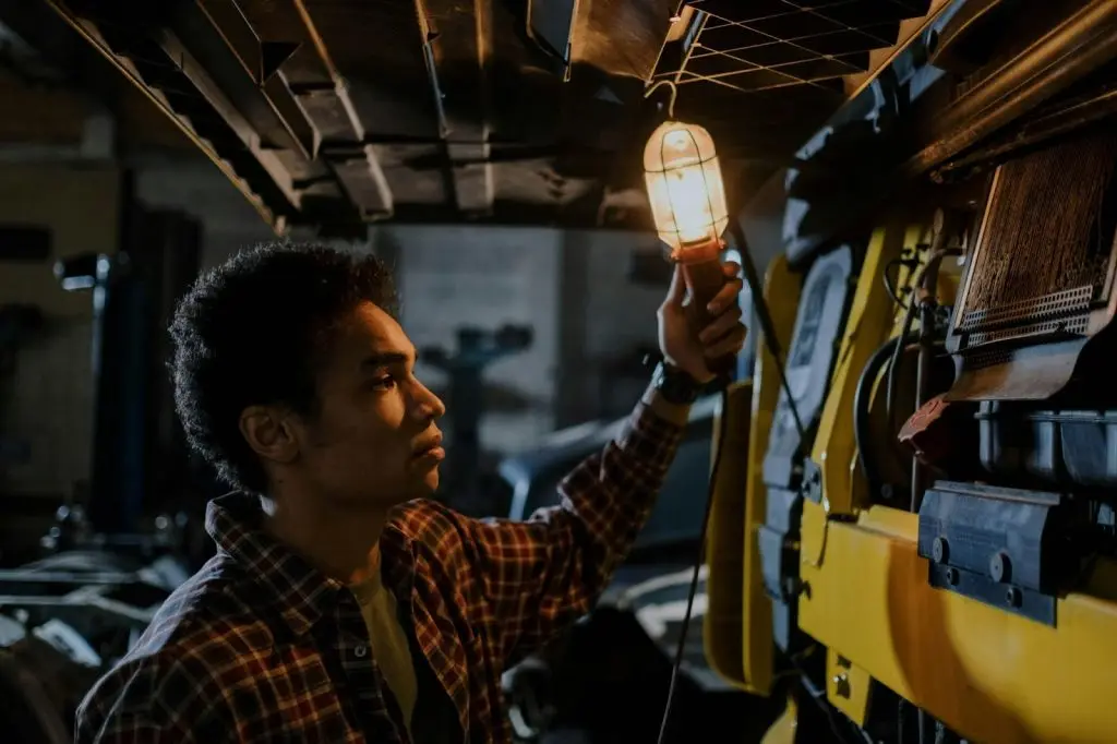 A truck owner performing a visual engine inspection using a light bulb to check for leaks during truck maintenance.