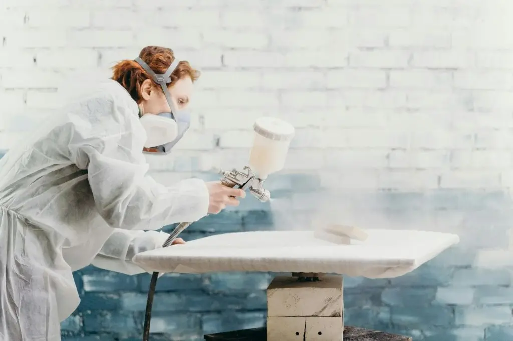 A close-up of a high-pressure airless spray gun with a clean fan pattern being demonstrated.