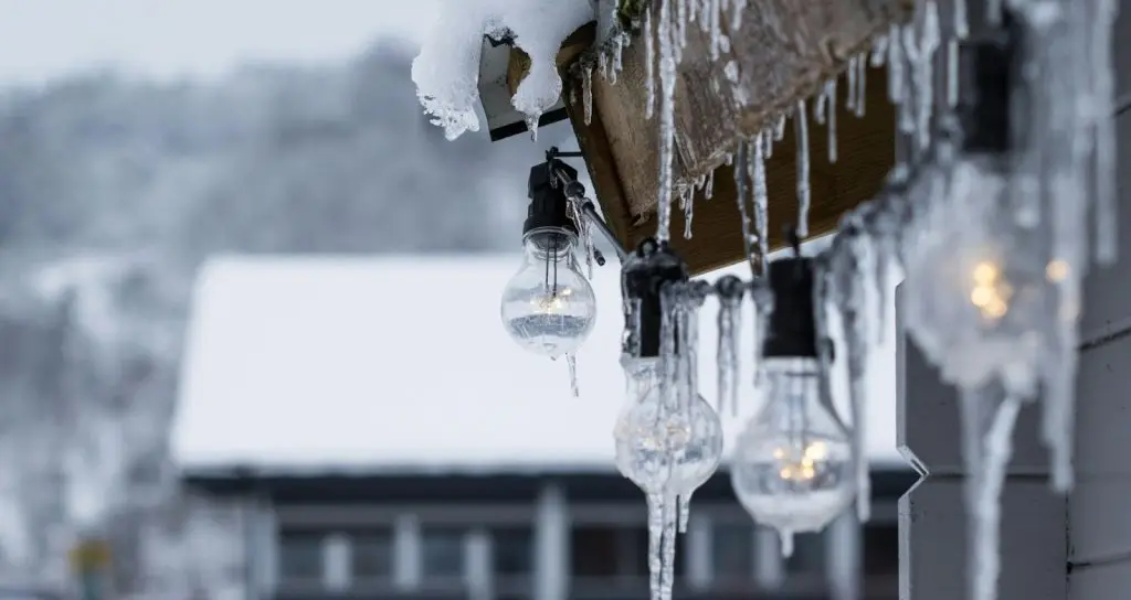 A close-up shot of several glass light bulbs hanging on a balcony, covered in frozen ice and icicles.