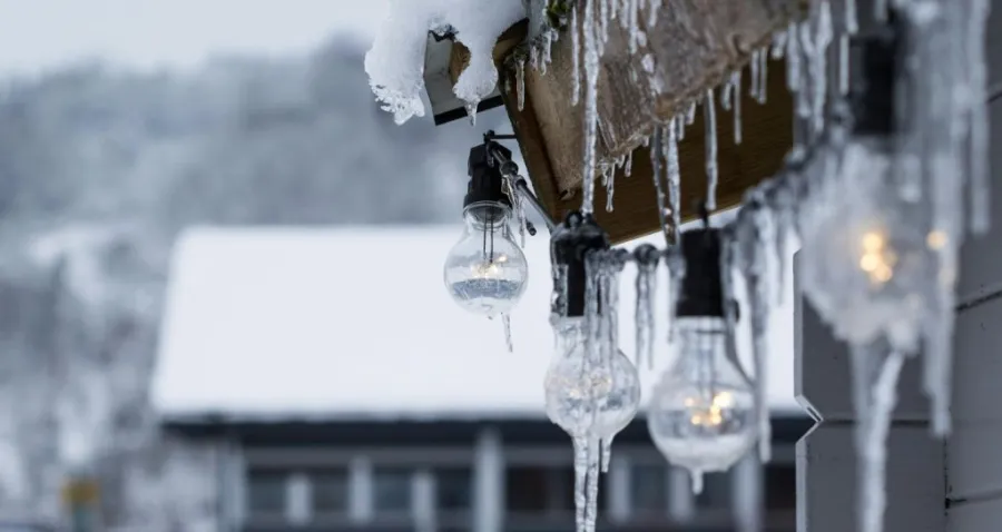 Eine Nahaufnahme von mehreren Glasglühbirnen, die an einem Balkon hängen und mit gefrorenem Eis und Eiszapfen bedeckt sind.