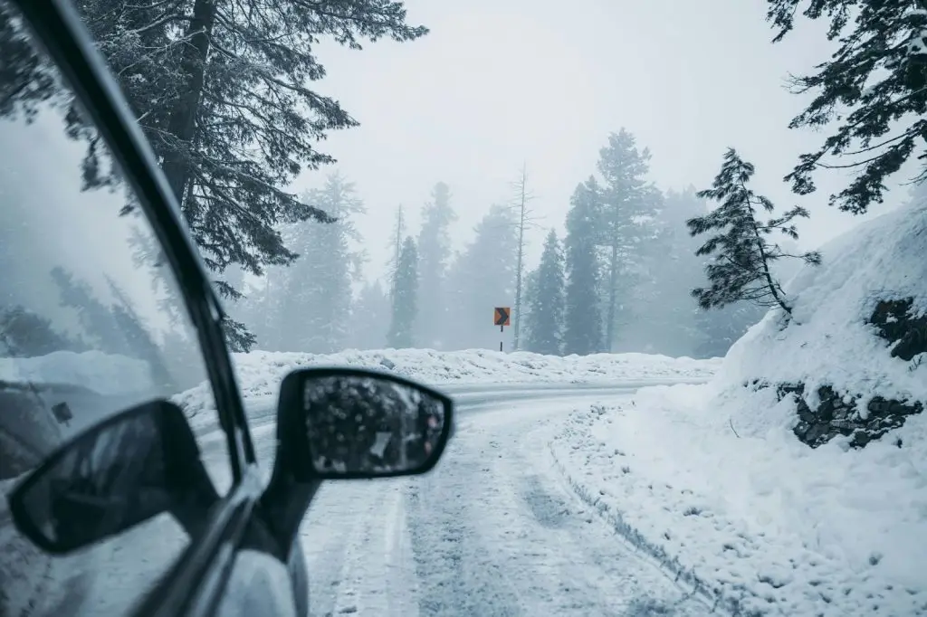 Nahaufnahme eines Autoaußenspiegels, der einer eleganten Kurve an einem schneebedeckten Berghang folgt. Sicherheitstipps für das Fahren im Winter.