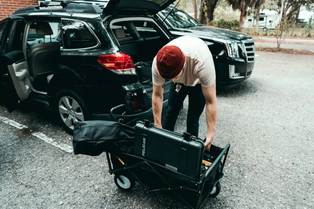 A man packing a portable power station into a box next to an open car trunk.