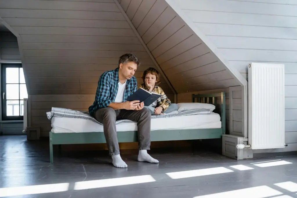 A father reading a book to his son in a room with a protective safety cover over the heater.