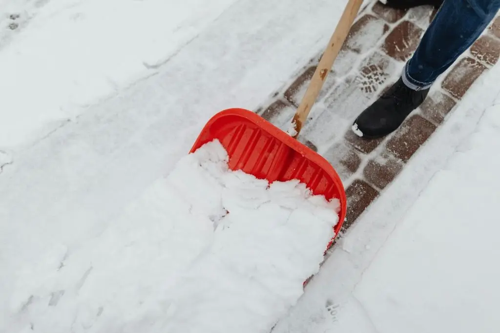 Close-up of a man using a shovel to clear a snow-covered walkway.