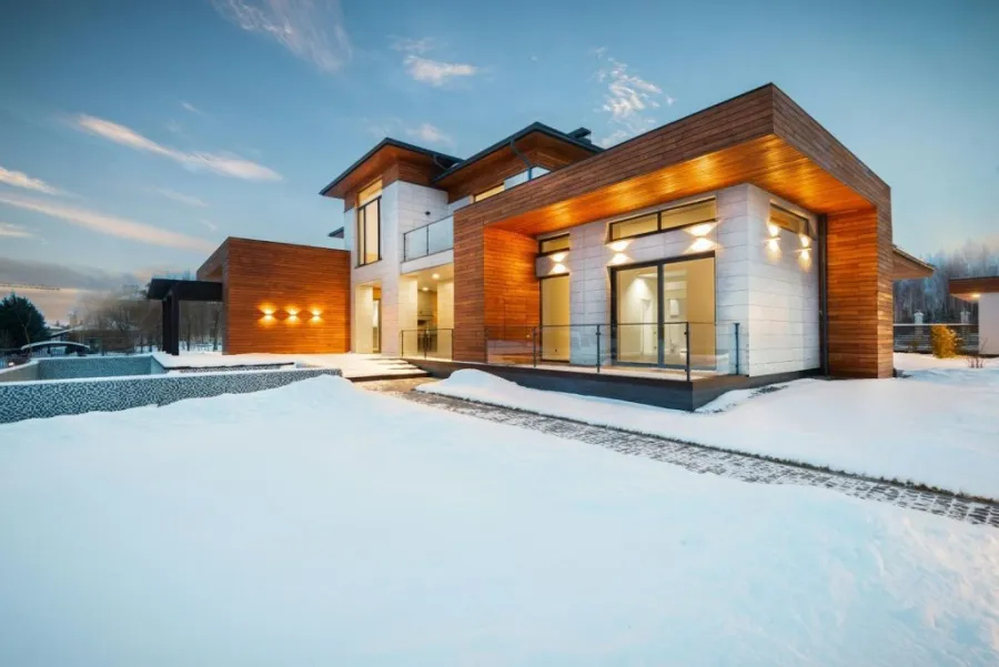 A warm-lit house at dusk surrounded by a blanket of snow in a winter landscape.