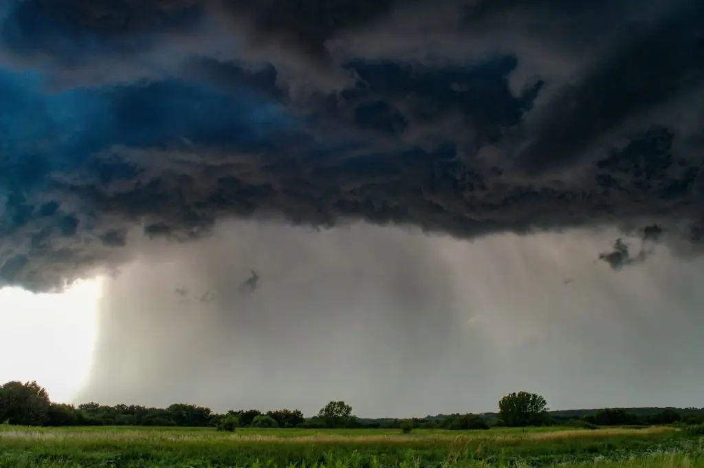 A landscape shot of dark clouds with heavy storm over lush green fields