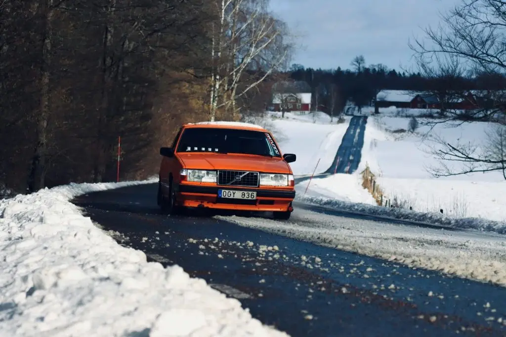 An orange car driving on a long, winding snowy road 