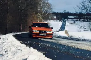 An orange car driving on a long, winding snowy road 