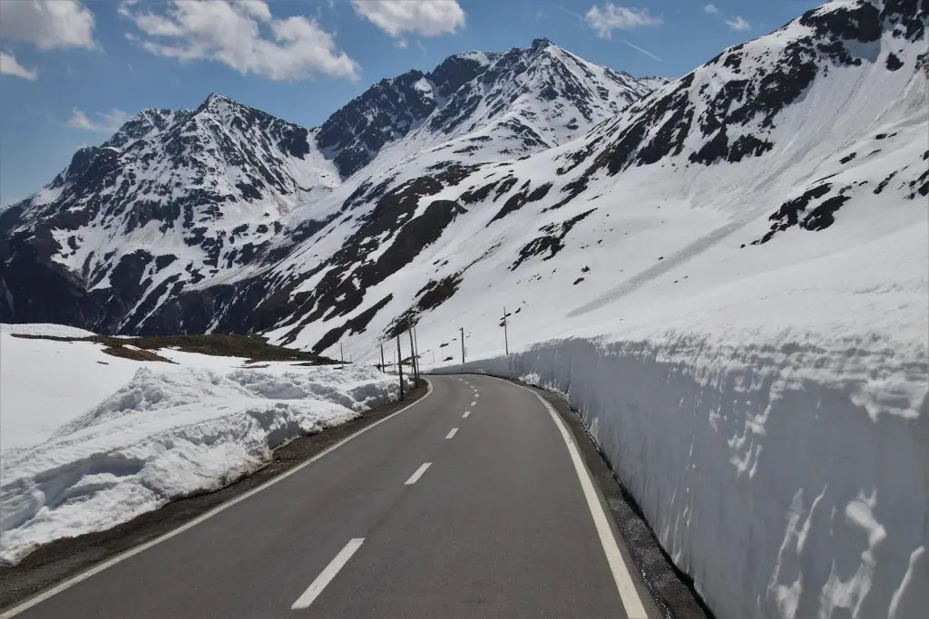 A clean, asphalt road stretching toward distant, snow-capped mountains under a clear sky.