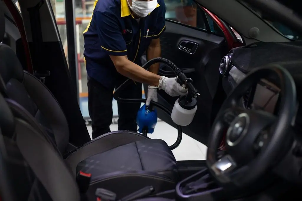 A man cleaning his vehicle by spraying a specialized rodent repellent for cars.