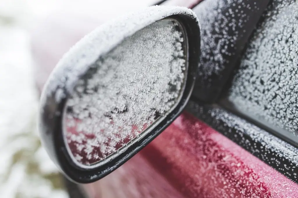 A close-up shot of a car's side mirror completely coated in a thick layer of ice