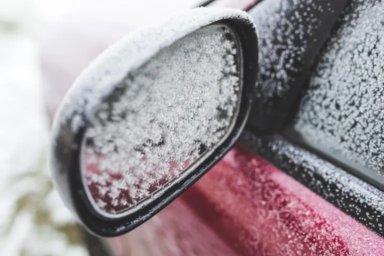A close-up shot of a car's side mirror completely coated in a thick layer of ice