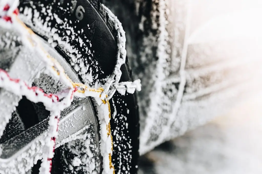 A close-up shot of a car tire completely covered in snow and wrapped in heavy-duty tire chains. how to store a car for winter