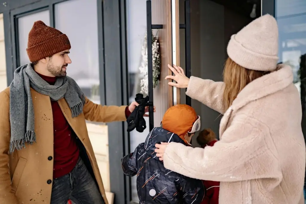 A family, including a man, woman, and child dressed in warm winter gear, entering their home