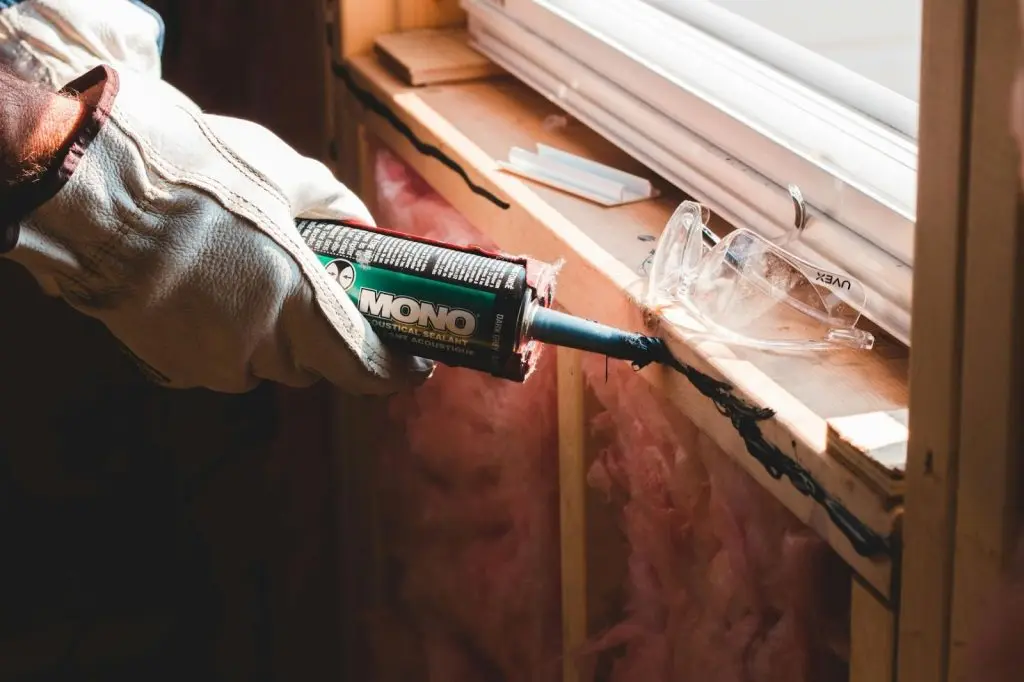 A close-up of a person applying a precise bead of caulk to a window frame using a manual gun.
