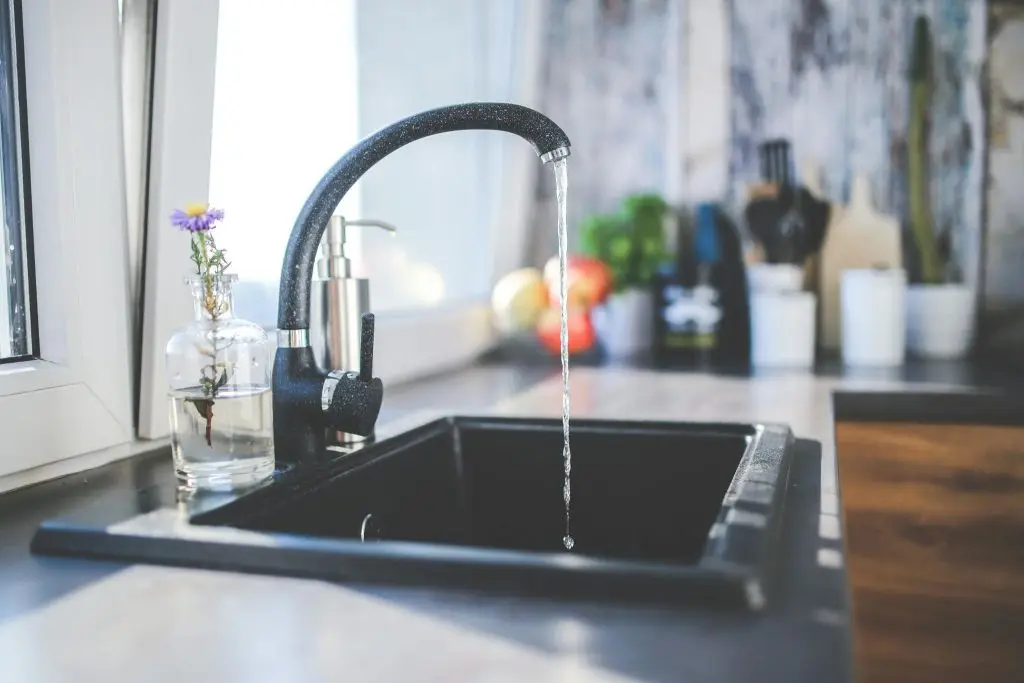 A close-up of a kitchen faucet with a weak stream of water dripping slowly into the sink.