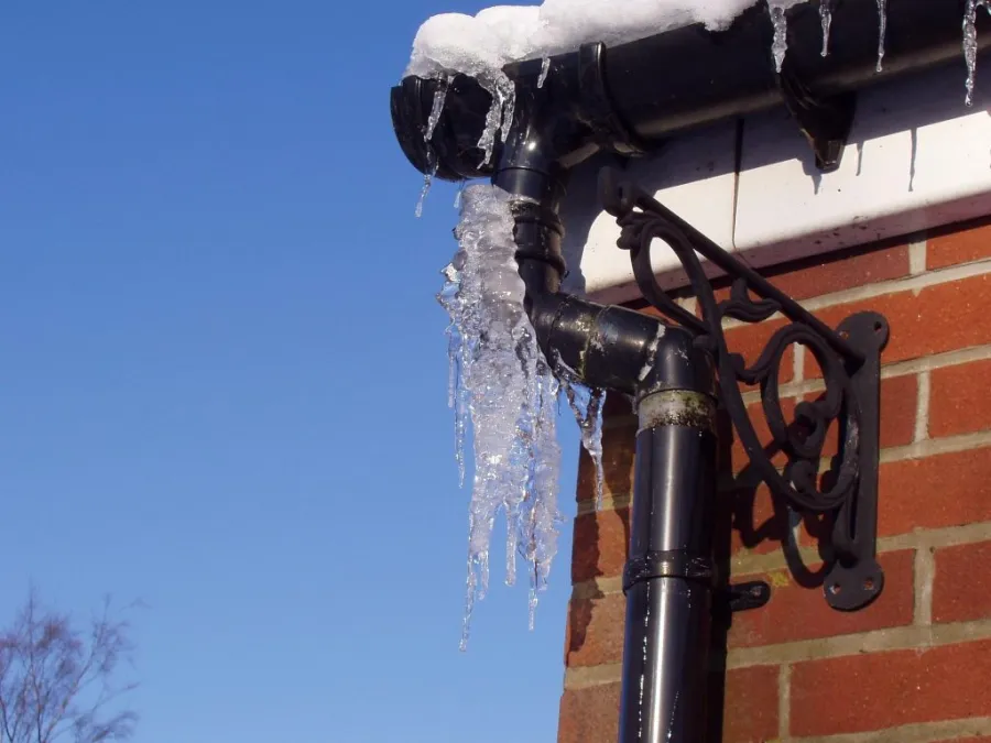 A cold, frosted metal pipe running along the outside of a brick wall covered with ice