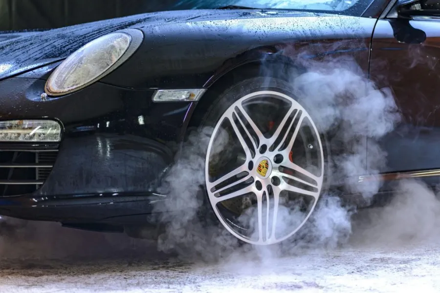 A close-up of a car tire drifting on asphalt with white smoke billowing from the rubber.