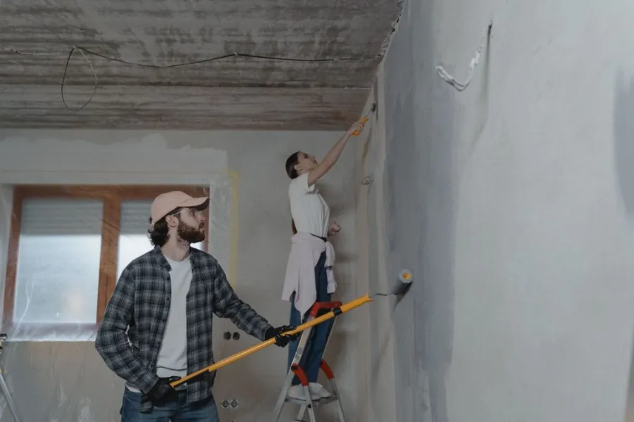 A man and a woman are undertaking basement repair by painting concrete basement walls.