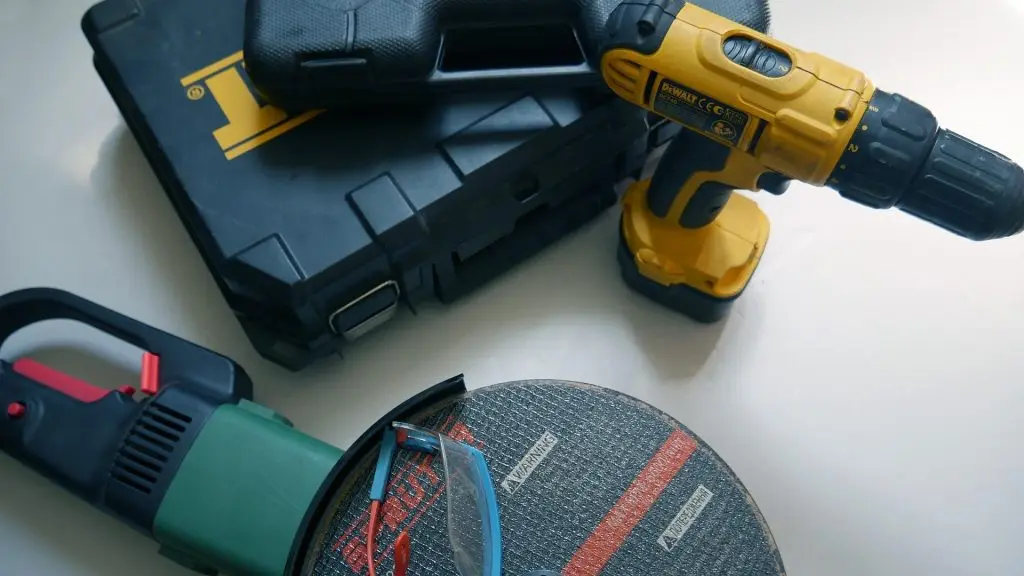 A home tool kit with a cordless drill, a retractable measuring tape, and clear protective glasses laid out on a flat surface.