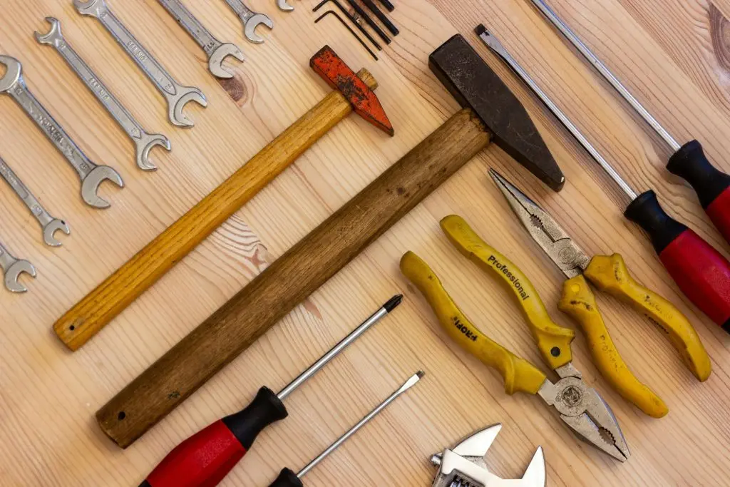 Various tools including a claw hammer, slip-joint pliers, and professional-grade wrenches spread out on a wooden workbench.