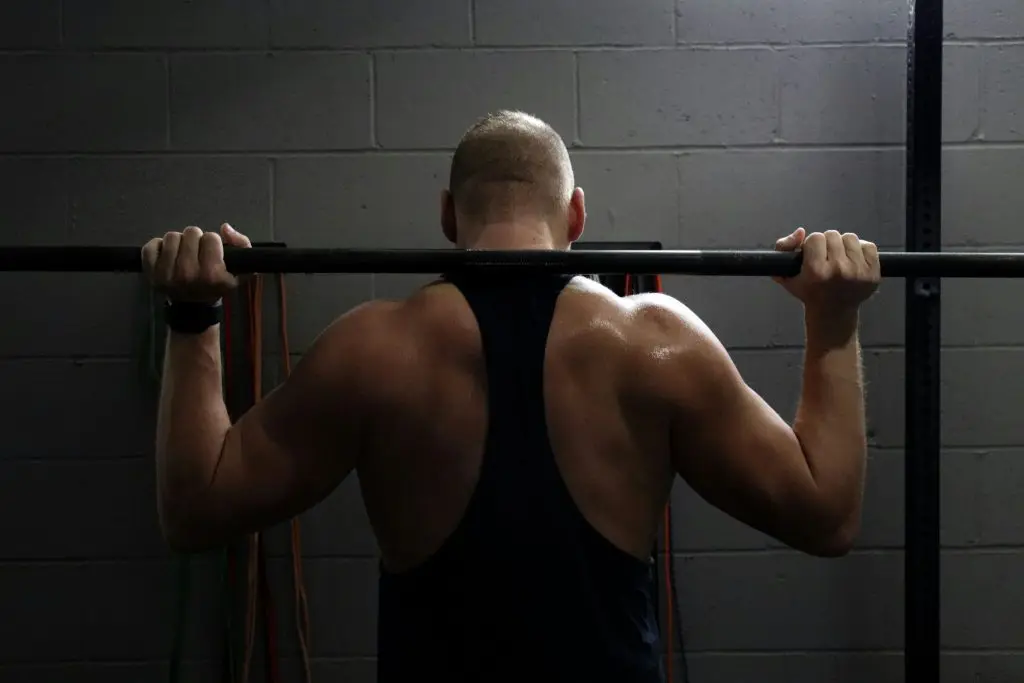 A man doing push-ups with the handles of a pull-up bar mounted on a brick wall.
