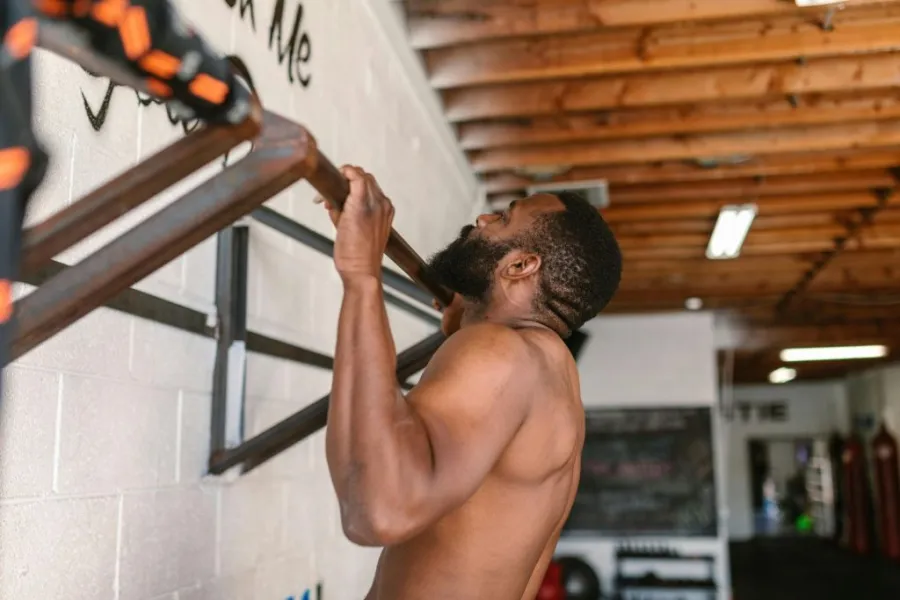 A man grabs a pull-up bar as he faces a wall-mounted gym setup.