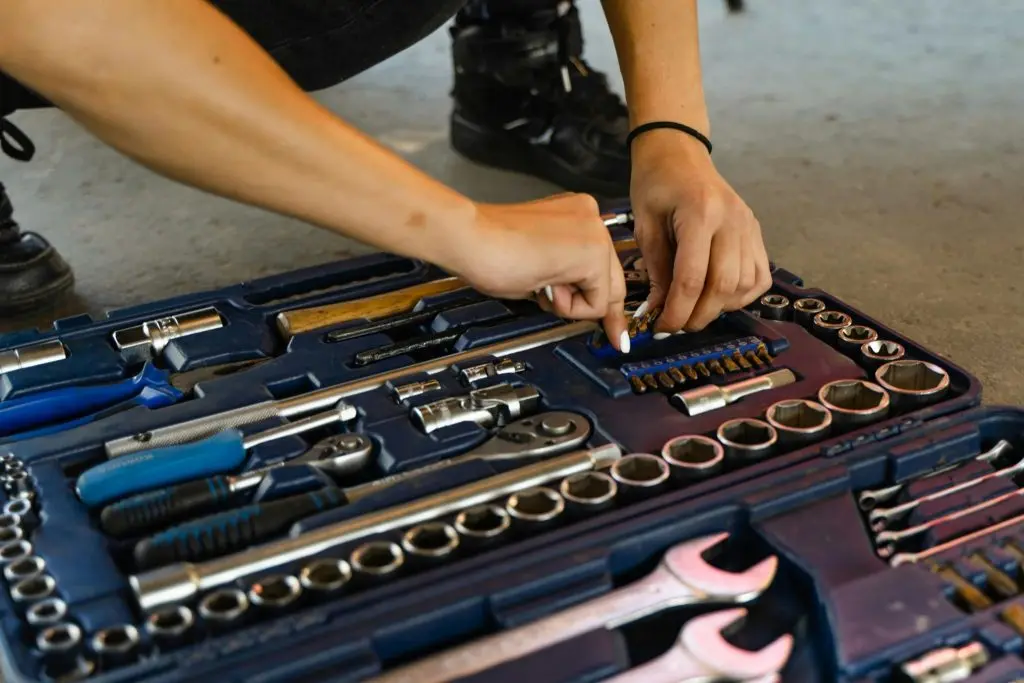 A close-up of a woman's hands neatly organizing various metal sockets in a professional storage container.