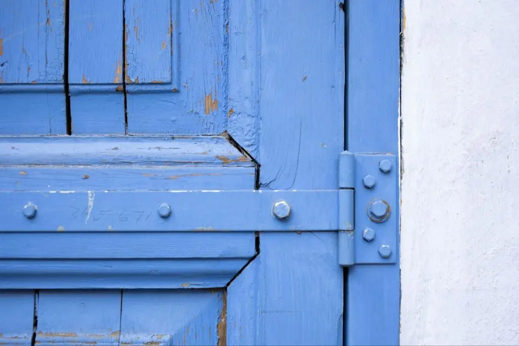 weathered blue wooden door featuring rusty hinges and peeling paint