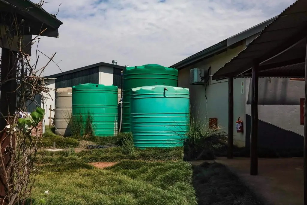 Tre grandi serbatoi d'acqua di colore verde, installati su una base di cemento livellata nel giardino erboso di un'abitazione privata.