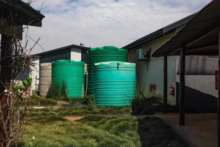 Three large green water storage tanks installed on a level concrete base in a grassy residential backyard.