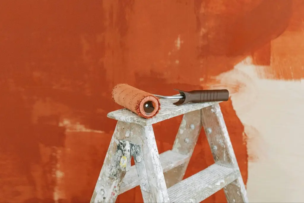 paint roller on a ladder with a partially painted red wall in the background