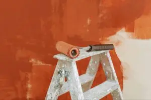 paint roller on a ladder with a partially painted red wall in the background