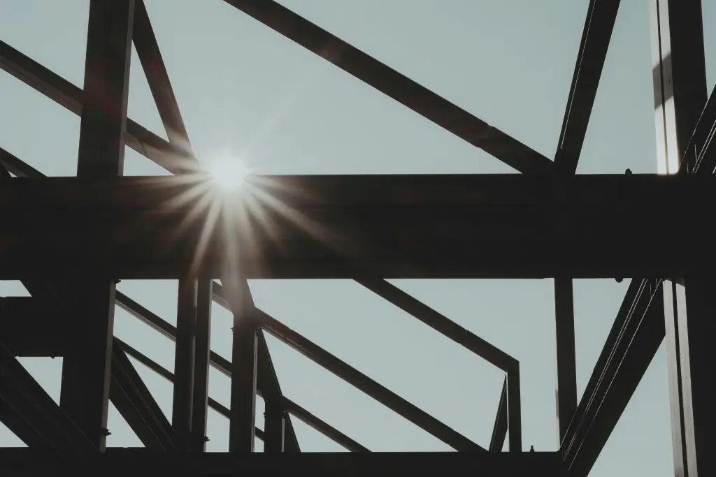Close-up of a dark steel beam structure with a bright sunset in the background.