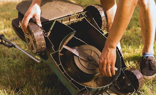 Tipping a mower on its side to remove the blade for bench grinder sharpening